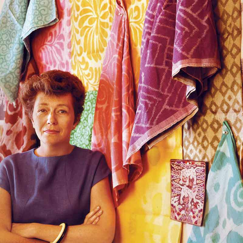Photograph of AIGA Medalist Gere Kavanaugh in front of a wall of colorful textiles