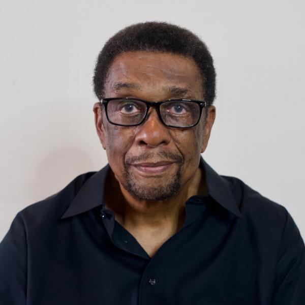Headshot of Archie Boston, Jr. wearing a black collar shirt and balck rimmed glasses.