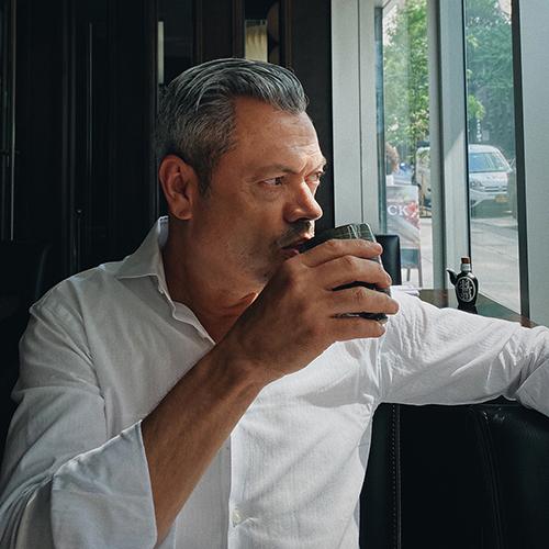 Color portrait of Rafael Esquer looking out the window drinking a cup of coffee
