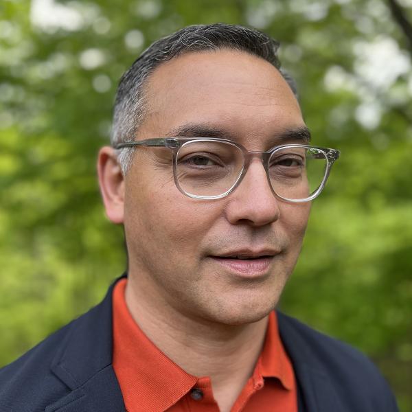 Headshot of 2022 AIGA Medalist Andrew Satake Blauvelt wearing a collar shirt and jacket and glasses against an outdoor setting. Image courtesy of Andrew Satake Blauvelt.