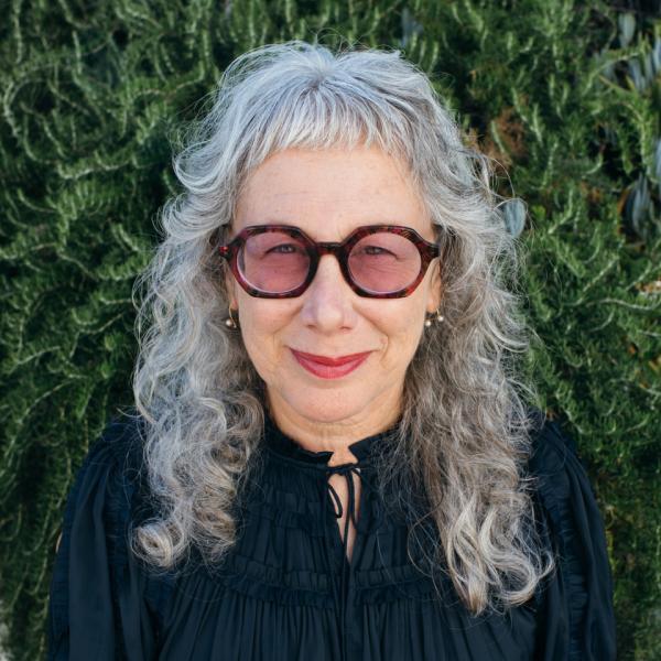 Headshot of 2022 AIGA Medalist Louise Sandhaus wearing a black top and sunglasses against an outdoor setting. Image courtesy of Louise Sandhaus. Photo credit: © Moira Tarmy